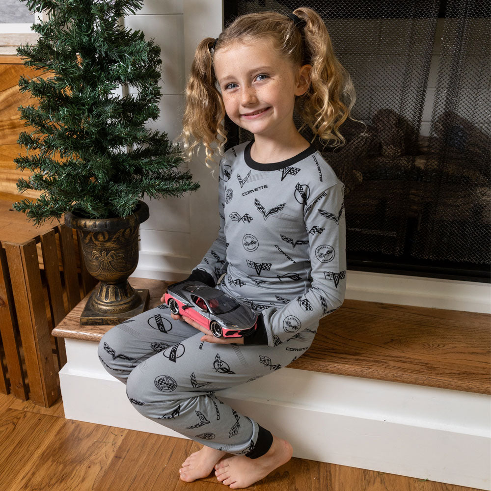 Youth sitting next to a fireplace wearing the Gray C1 through C8 Corvette Emblems Print Youth Pajama Set