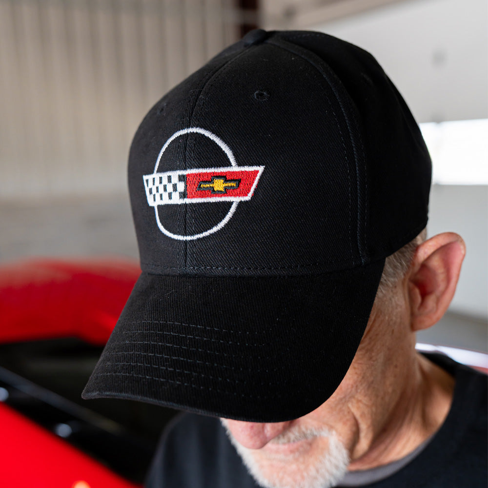 Black cap with a C4 Corvette logo worn by a person in front of a red Corvette.