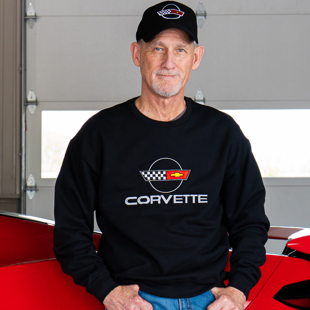 Man wearing a black C4 Corvette sweatshirt and cap in front of a red Corvette.