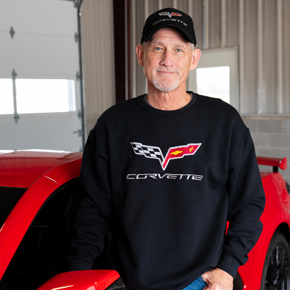 Man wearing a black Corvette sweatshirt and cap in front of a red Corvette.