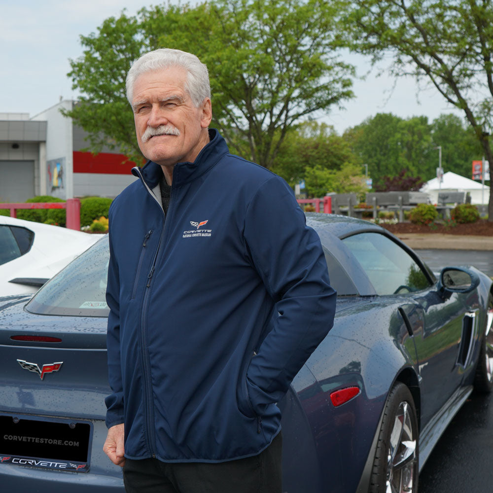 Man wearing the C6 Corvette Trail Softshell Navy Jacket standing in front of a blue C6 Corvette