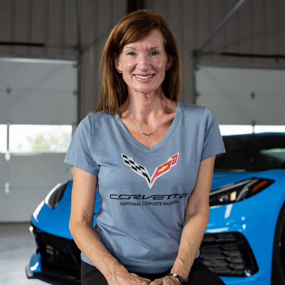 Woman wearing a C7 Corvette t-shirt sitting in front of a blue Corvette in a garage.