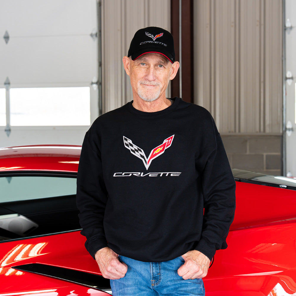 Man wearing a black Corvette sweatshirt and cap standing in front of a red Corvette car.
