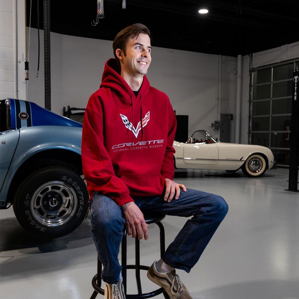 Man sitting on a stool in a garage wearing the C7 Corvette Fundamental Fleece Crimson Red Hoodie