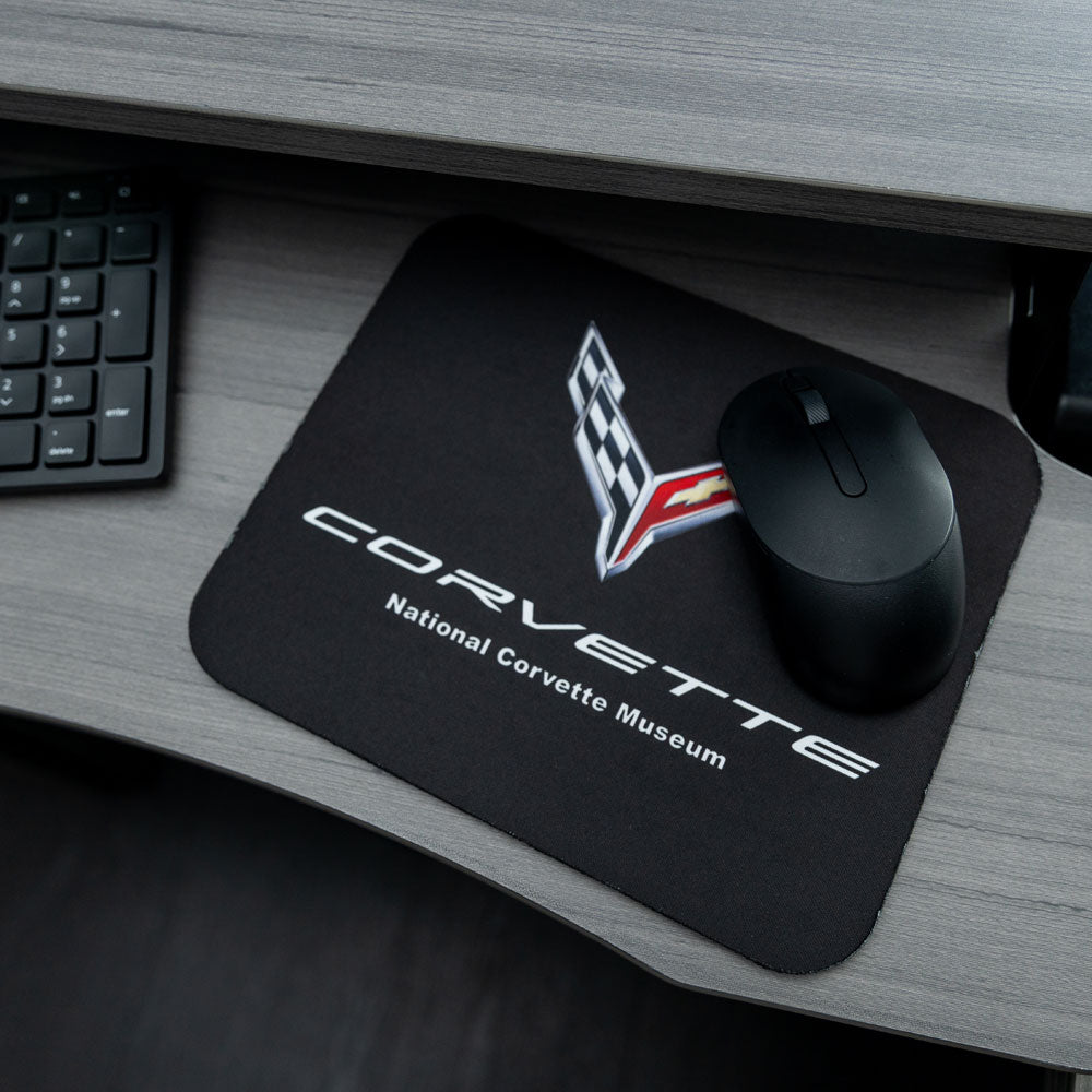 The C8 Corvette Emblem Black Mouse Pad shown placed on a desk  next to a keyboard