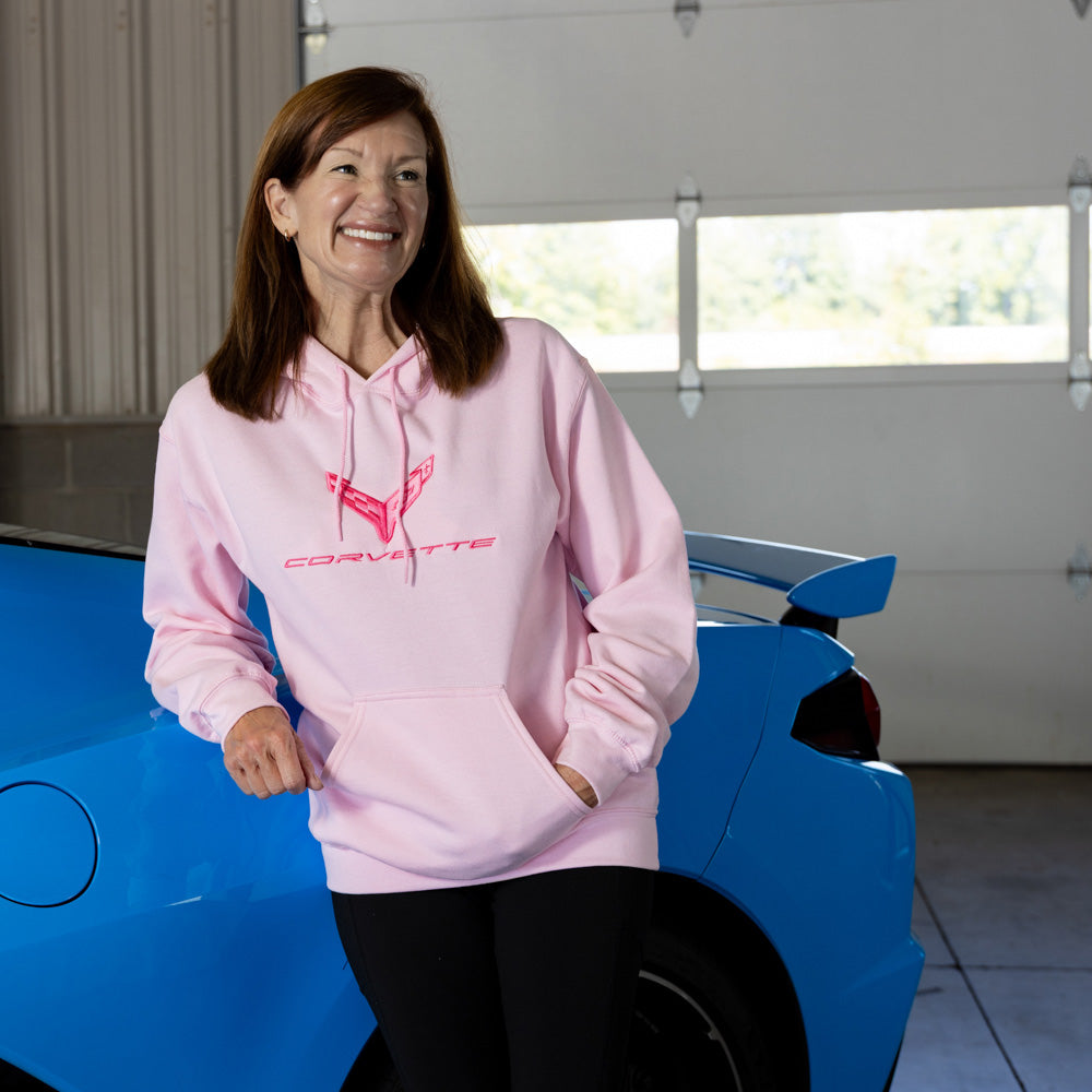 Woman wearing a pink C8 Corvette sweatshirt standing next to a blue Corvette