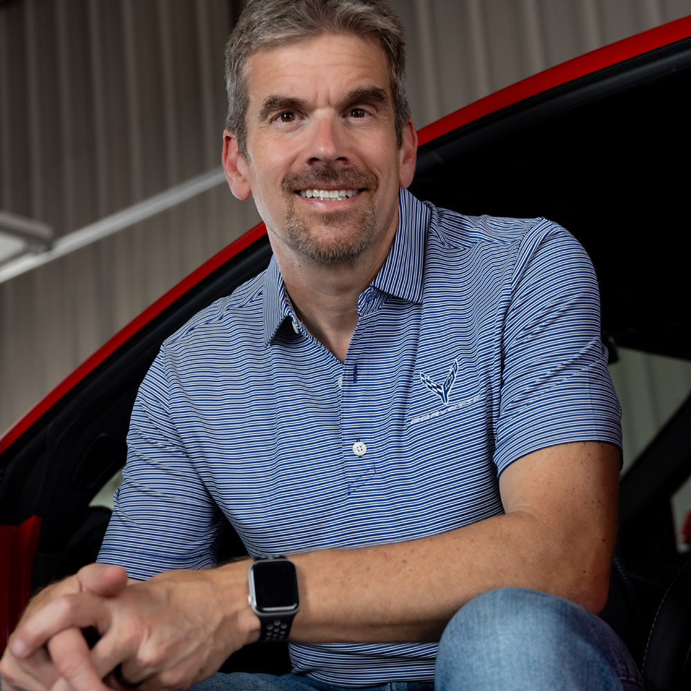 Man sitting in a Corvette wearing the C8 Corvette Forge Double Stripe Royal Blue and White Polo