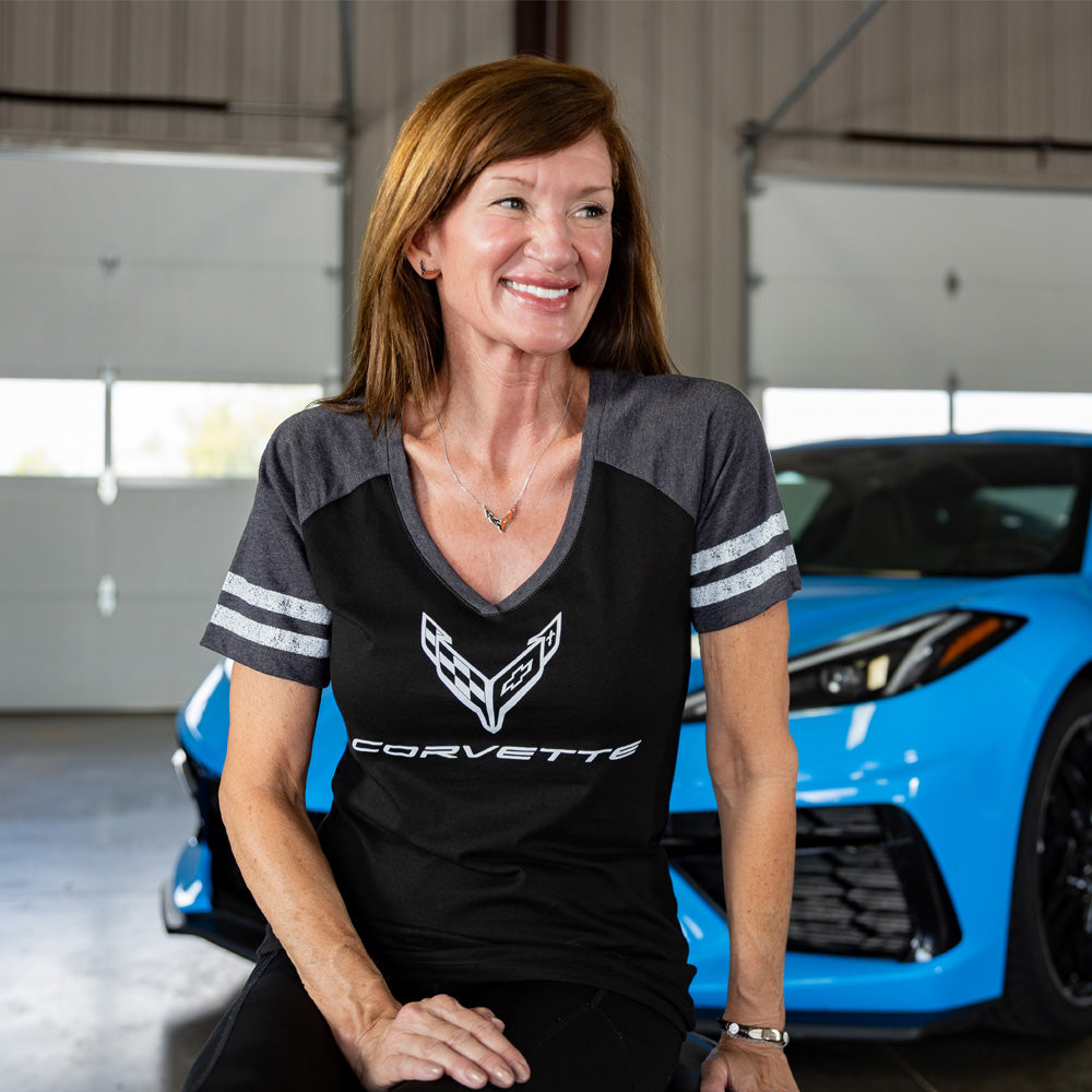 Woman wearing a C8 Corvette tee sitting in front of a blue Corvette in a garage.