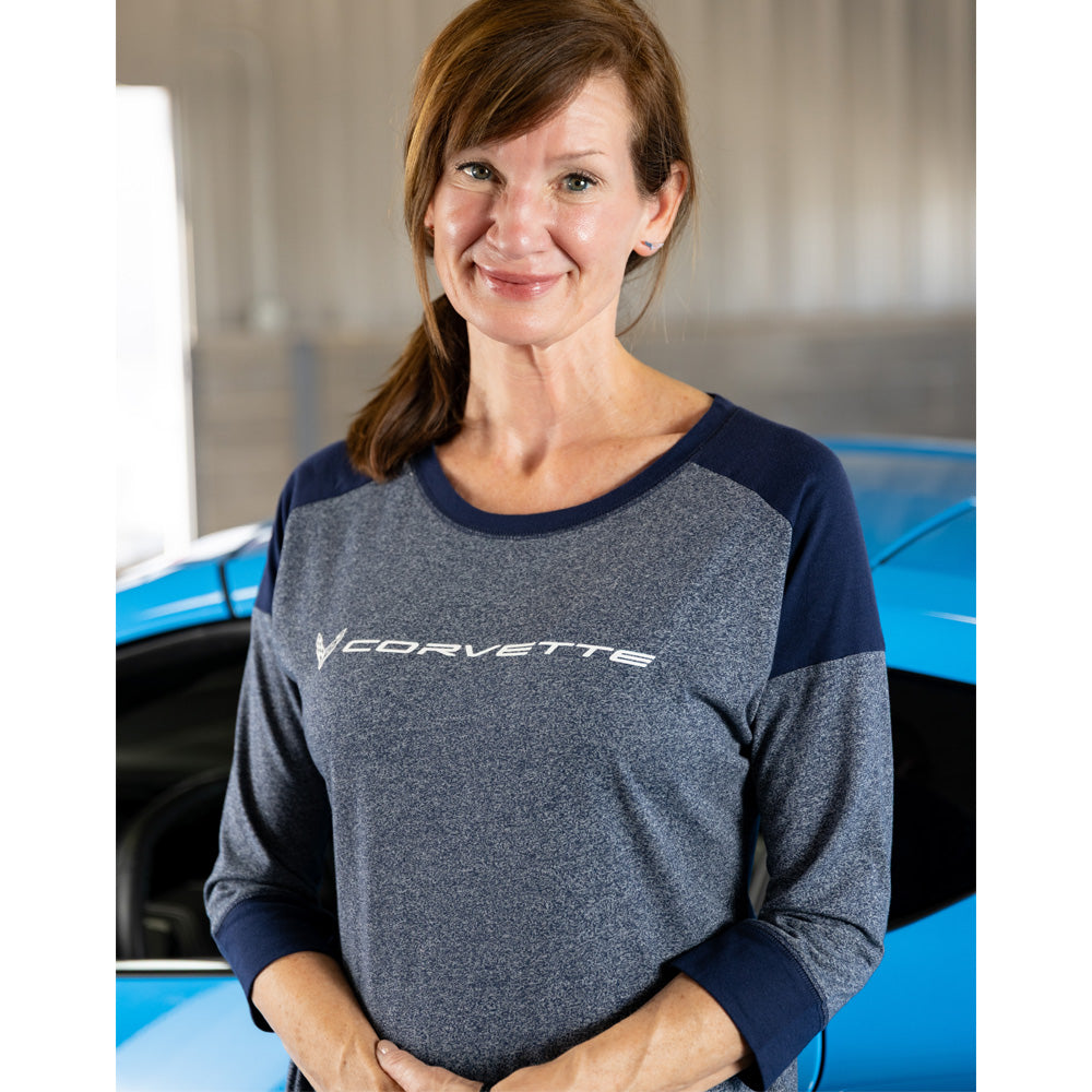 Woman wearing a blue Corvette three quarter sleeve base top standing in front of a blue Corvette