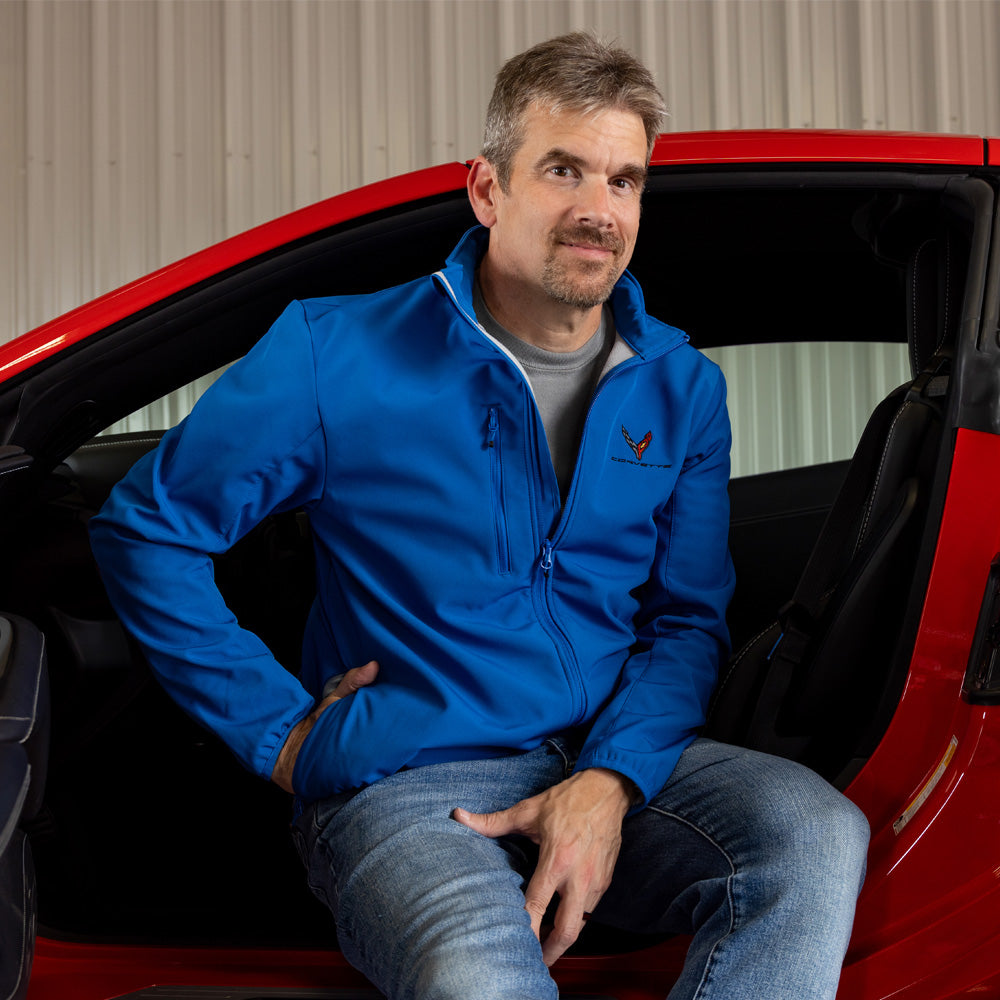 Man in a blue C8 Corvette jacket sitting inside a red Corvette.