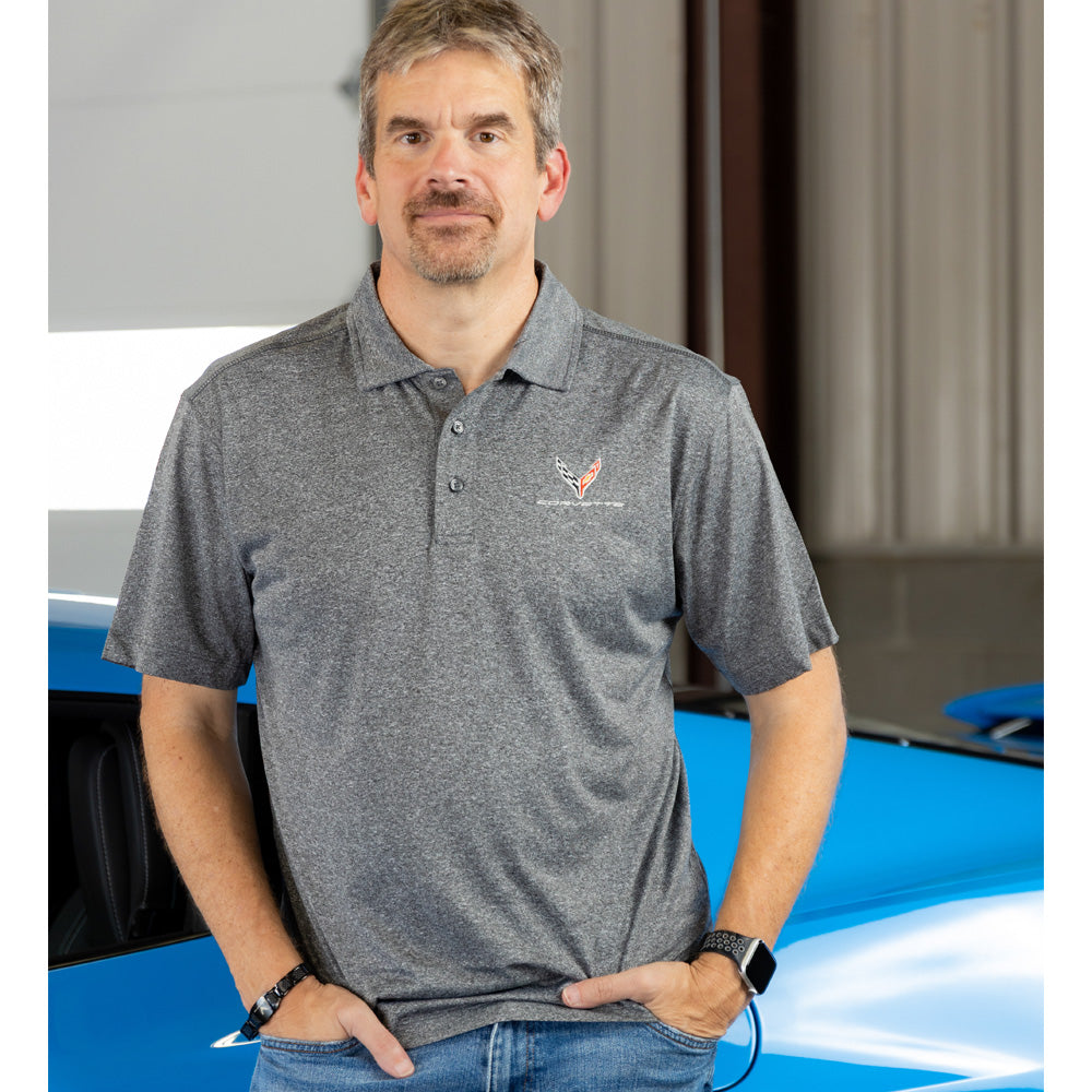 Man wearing a heather black polo shirt with a C8 logo, standing in front of a blue Corvette.