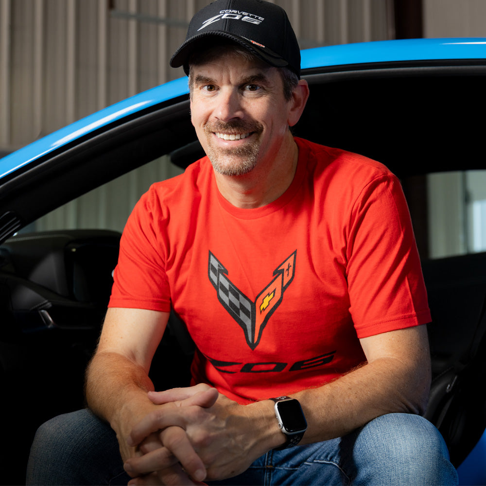 Man wearing a red C8 Z06 tee while sitting in a blue Corvette.