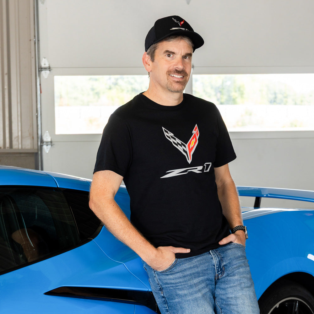 Man wearing a black Corvette t-shirt with a C8 ZR1 logo, standing next to a blue Corvette.