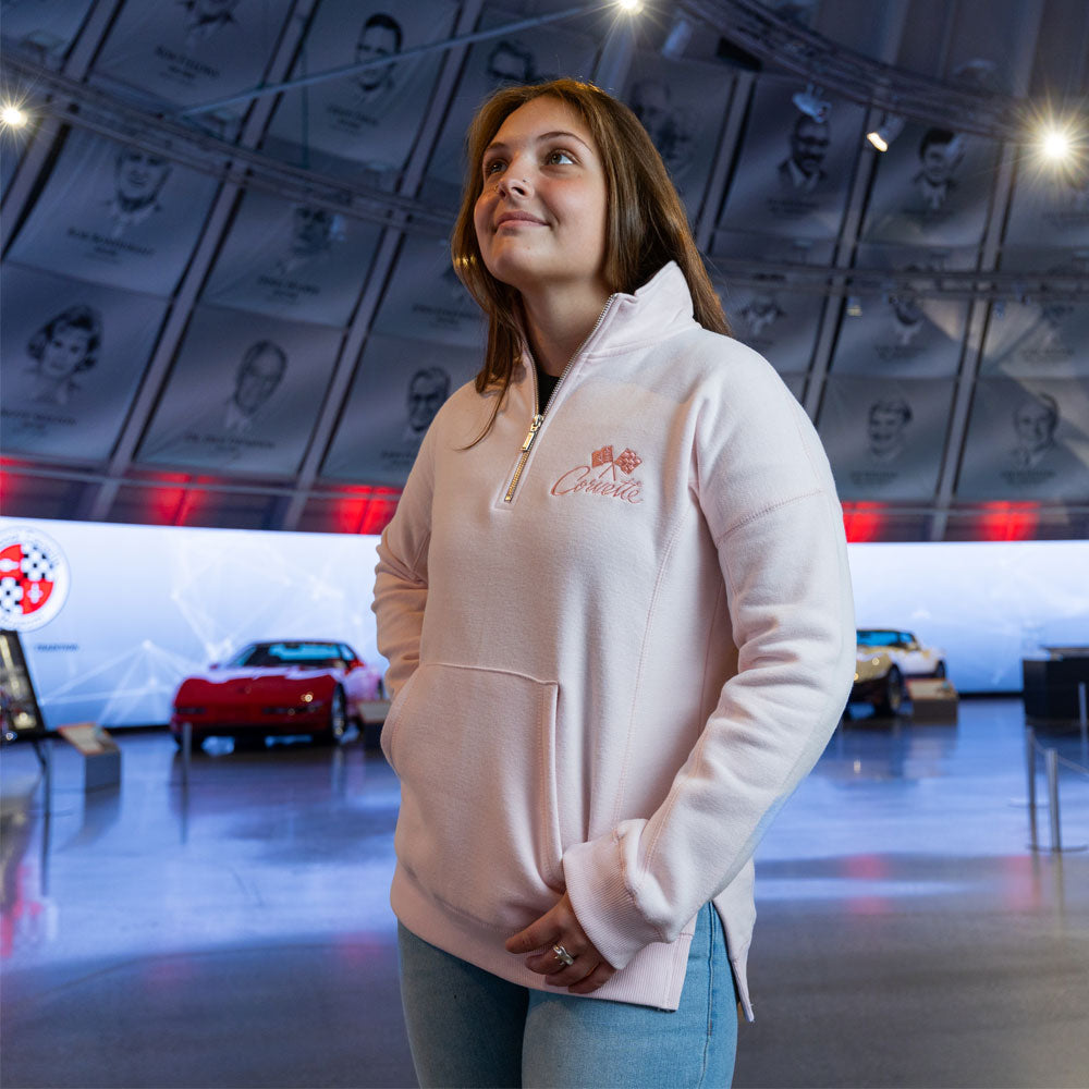 Woman standing in the Corvette Museum wearing the Corvette Crossed Flags Ladies Light Pink Quarter-Zip