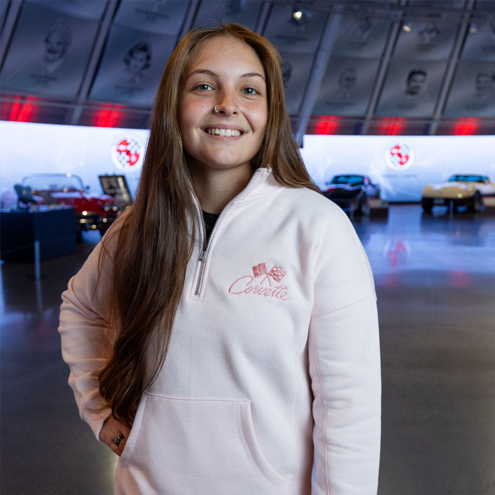 Woman standing in the Corvette Museum wearing the Corvette Crossed Flags Ladies Light Pink Quarter-Zip Pullover