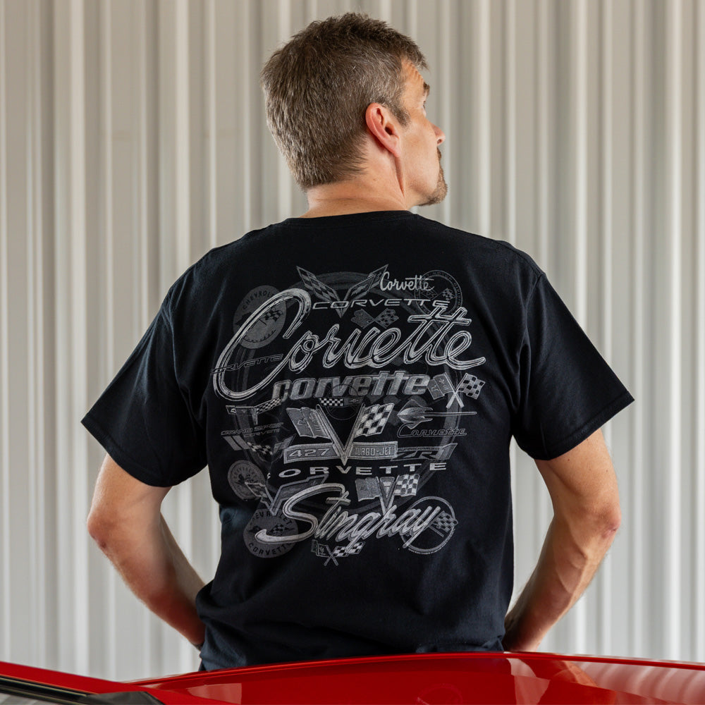 Man wearing a black Corvette t-shirt with a collage of Corvette emblems on the back, standing next to a red Corvette.