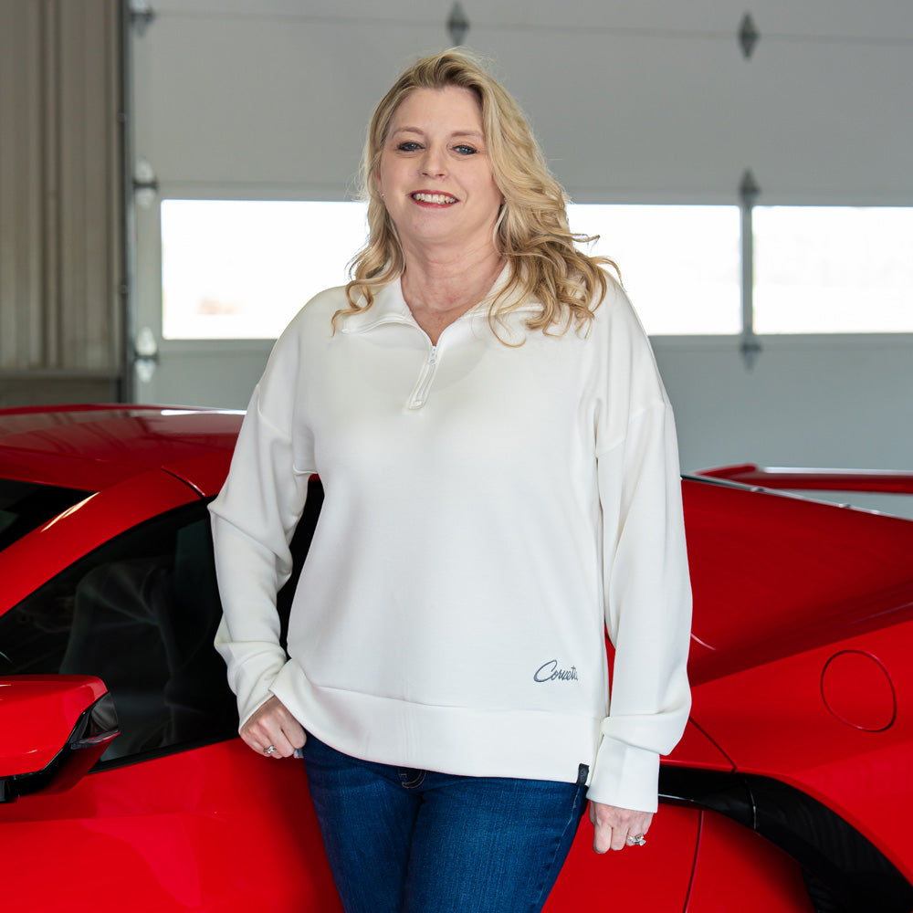 Woman wearing the Corvette Embroidered Script Quarter-Zip Pullover in White standing in front of a red Corvette