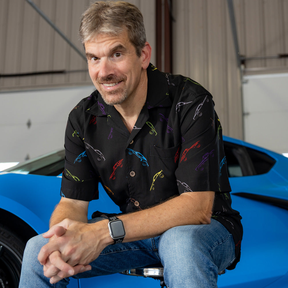 Man wearing a black camp shirt with Corvette silhouettes done in different colors