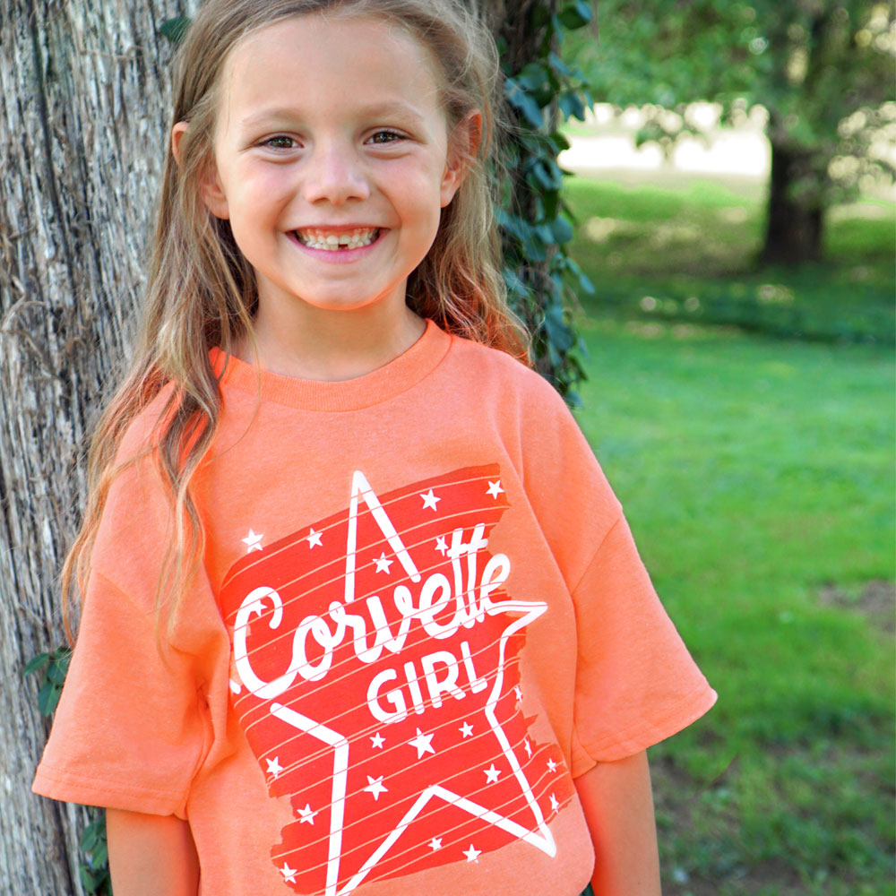 Little girl standing in a park wearing the Corvette Girl Starstruck Childrens Orange T-shirt