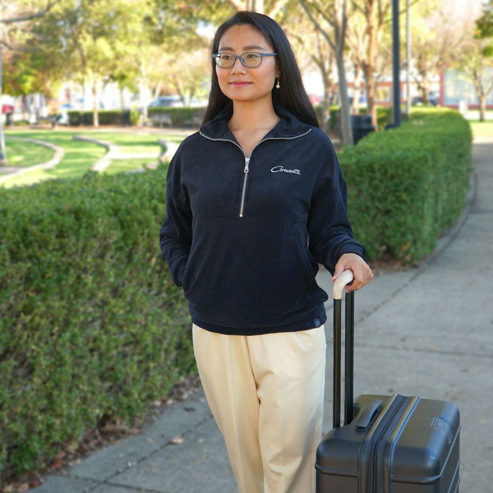 Woman wearing the Corvette Ladies Corded Half-Zip Black Pullover while wheeling a piece of luggage