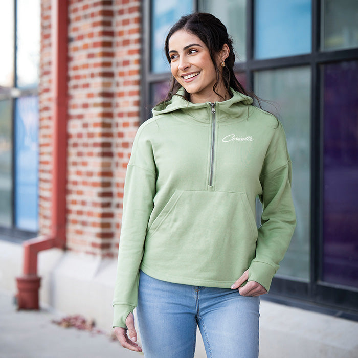 Woman wearing a light green hoodie with a Corvette script logo, standing outdoors.