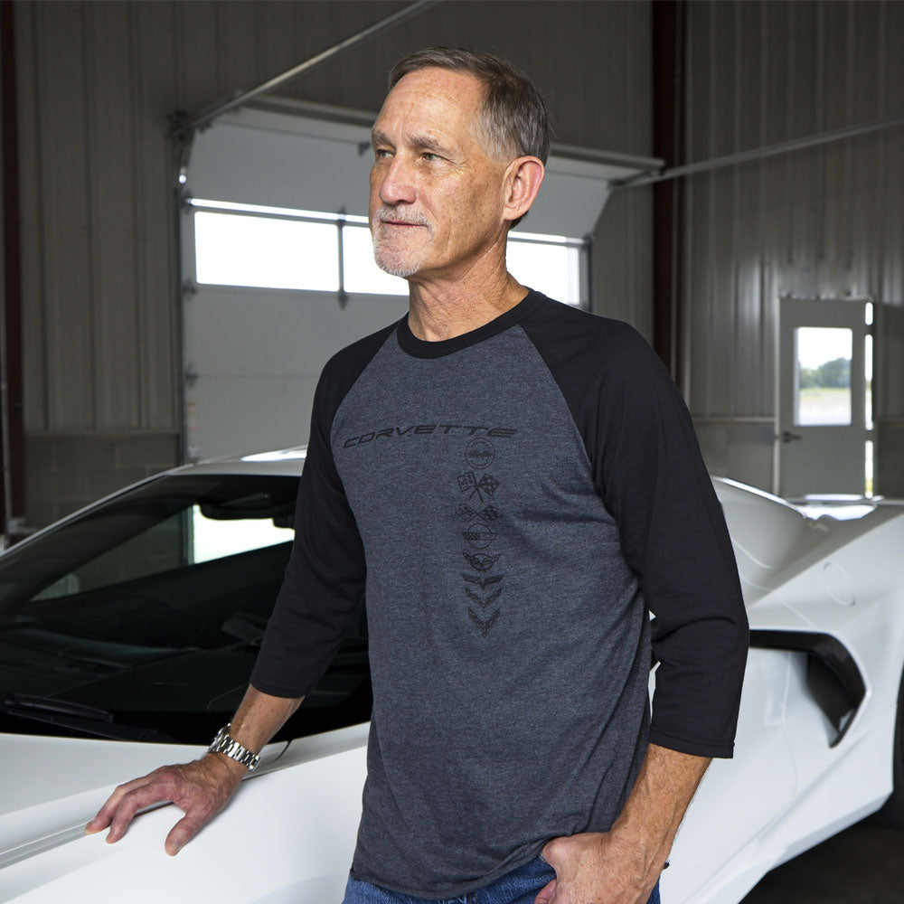 Man standing next to a White Corvette wearing the Corvette Multi Emblem Distressed Baseball Jersey in Black and Charcoal.