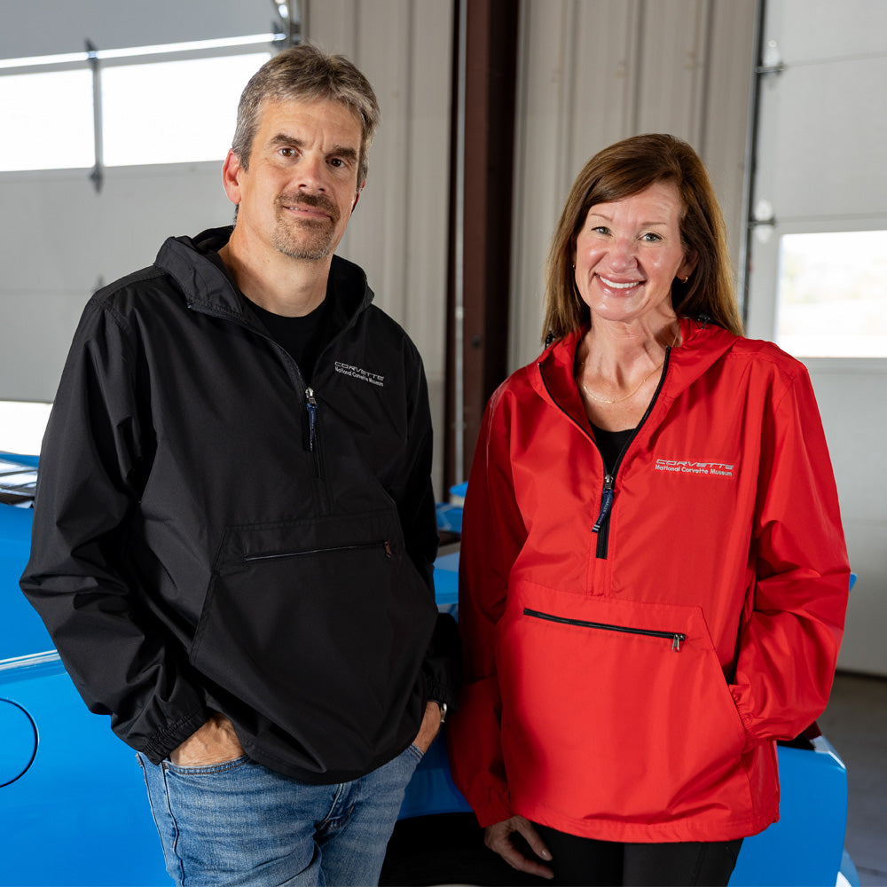 Two people wearing Corvette windbreakers standing in front of a blue Corvette.