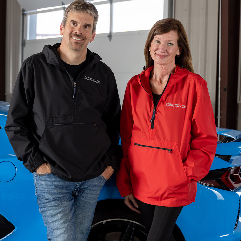 Two people, a man and a woman, standing in front of a blue Corvette wearing Corvette windbreakers