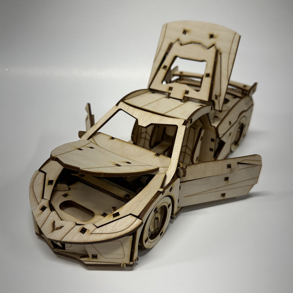 Wooden model car kit of a C8 Corvette shown with the doors and hood open on a white background