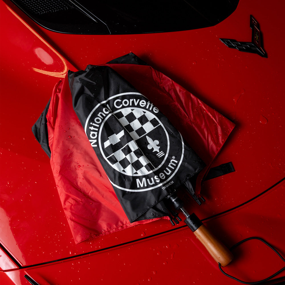 Black and red National Corvette Museum umbrella laying folded up on a red Corvette