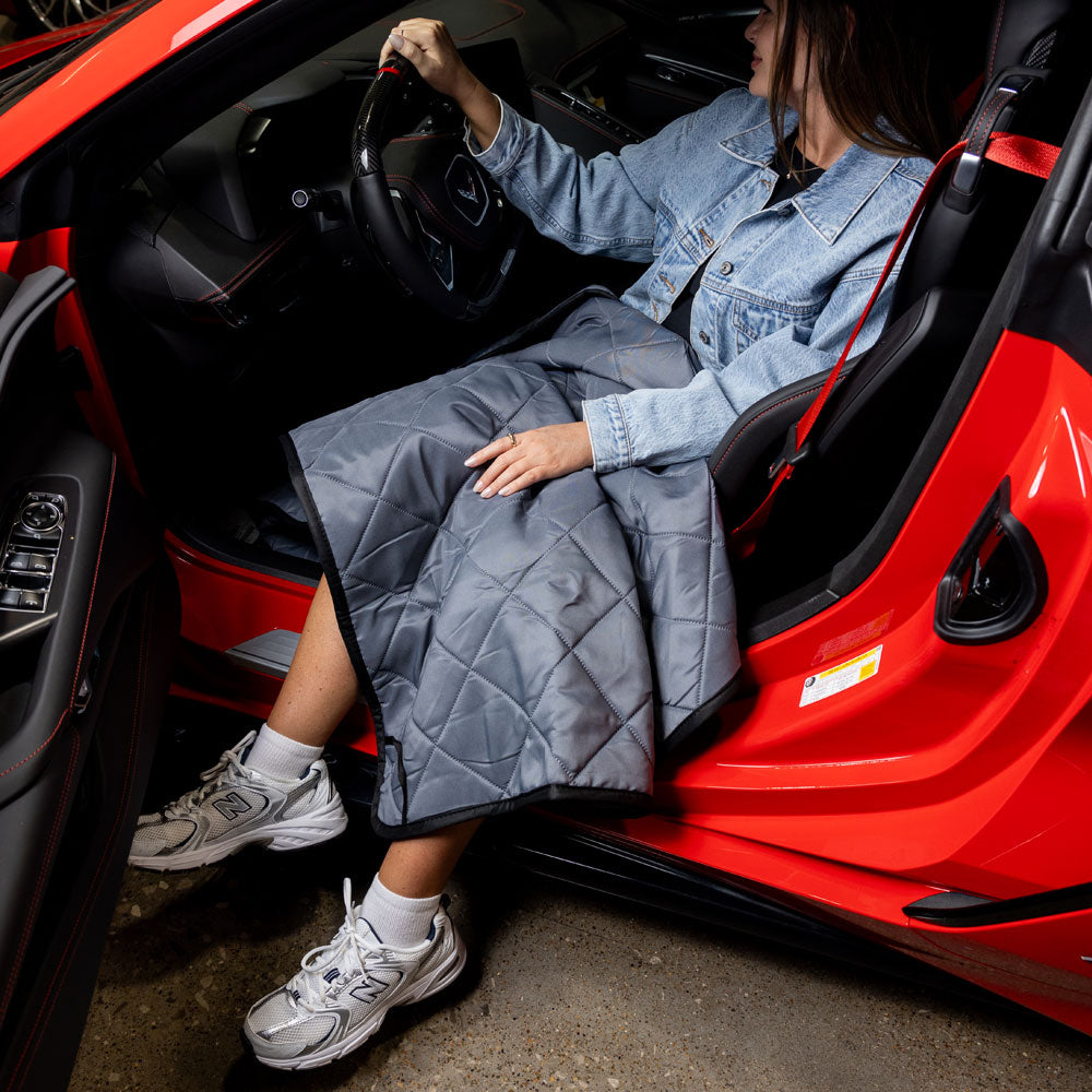 Woman sitting in a Corvette with the R8C Delivery Travel Blanket spread out over her lap