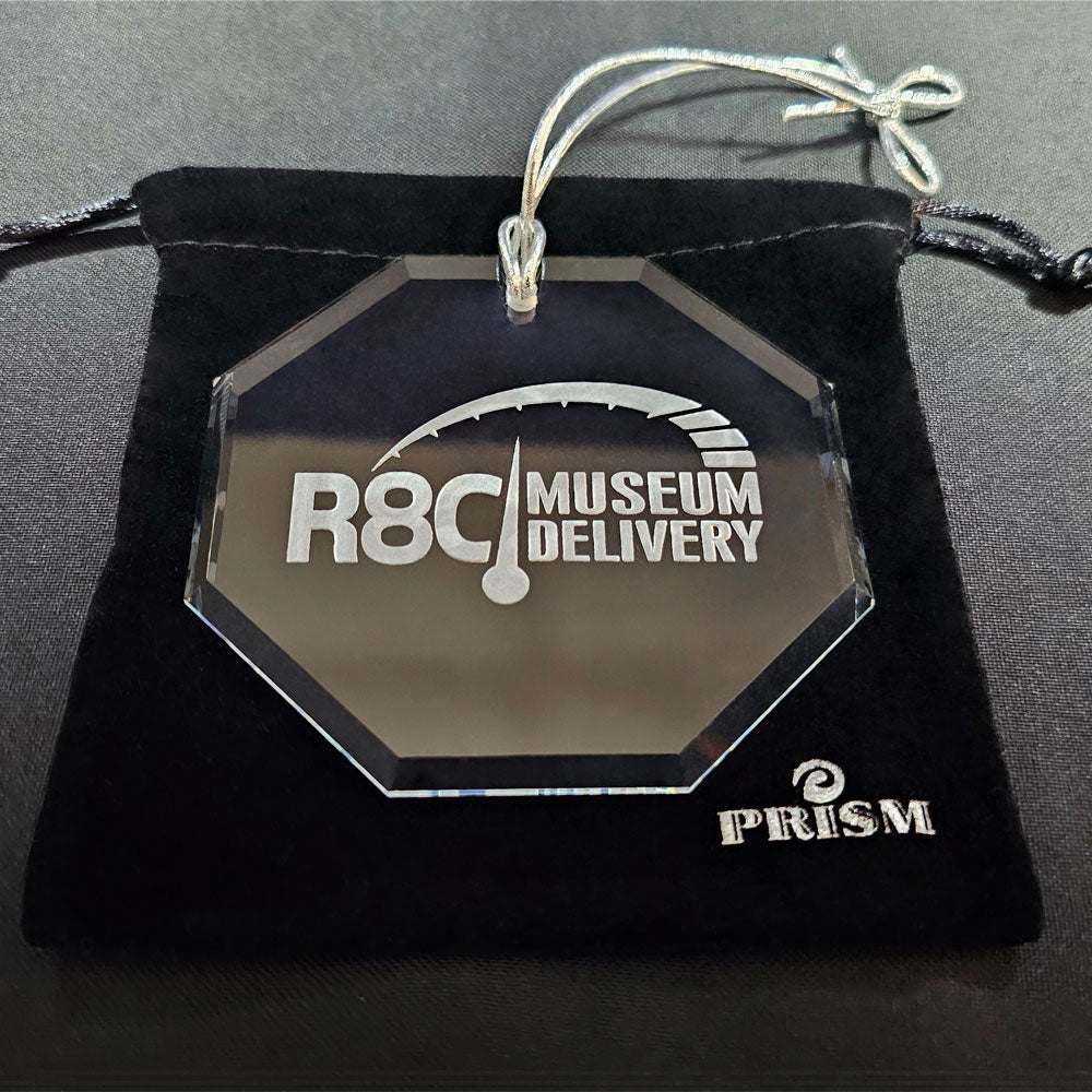 Hexagonal crystal ornament with 'R8C Museum Delivery' and 'PRISM' branding on a black velvet bag.
