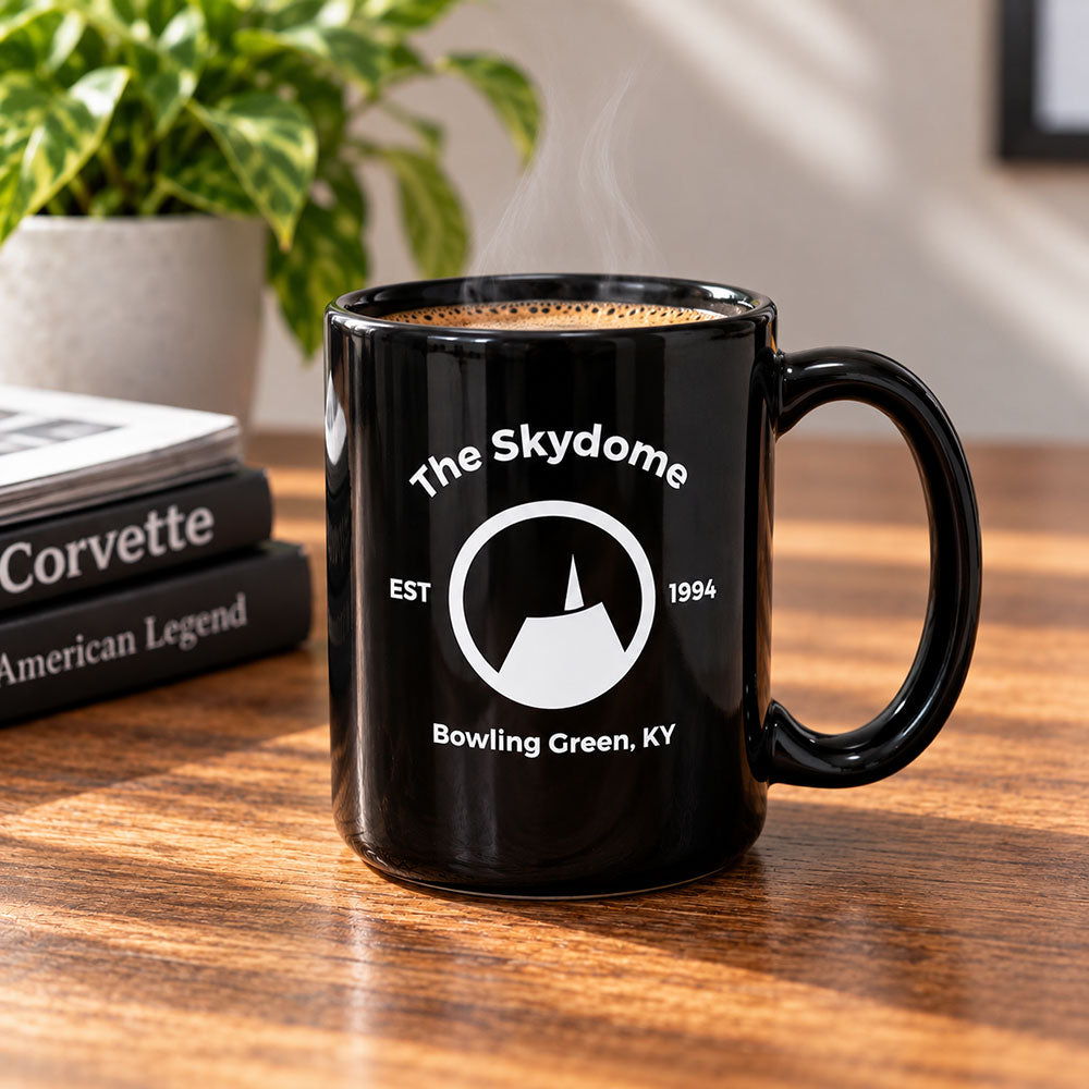 The Skydome of Bowling Green Black Mug shown sitting on a table next to some Corvette coffee table books.